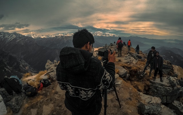 Muž v pletenom svetri, fotografuje ľudí na vrchole hory