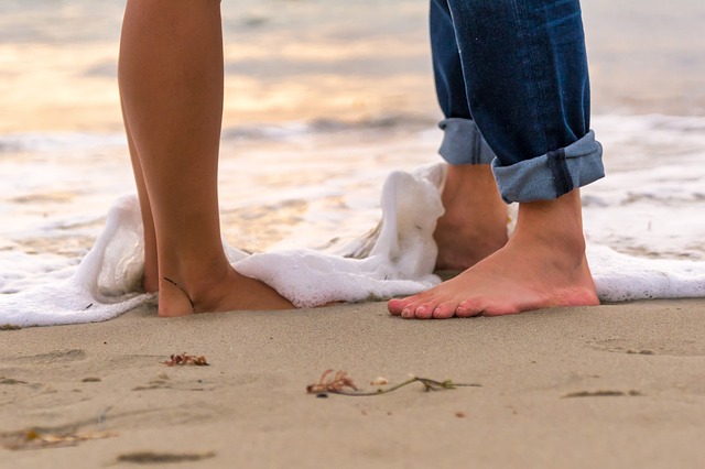 Muž a žena stoja s bosými nohami v prílive na pláži.jpg