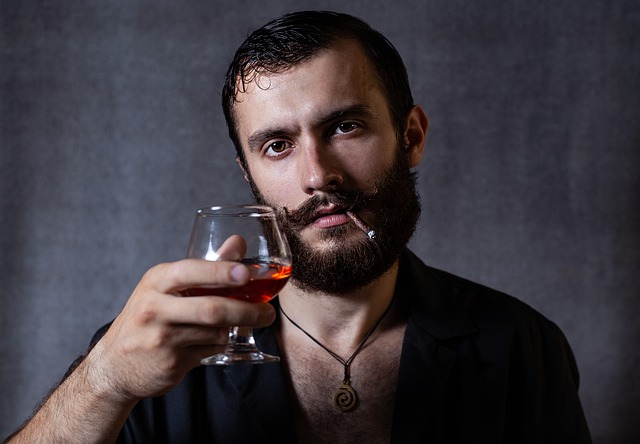 Muž s bradou drží v ruke pohárik s alkoholom.jpg